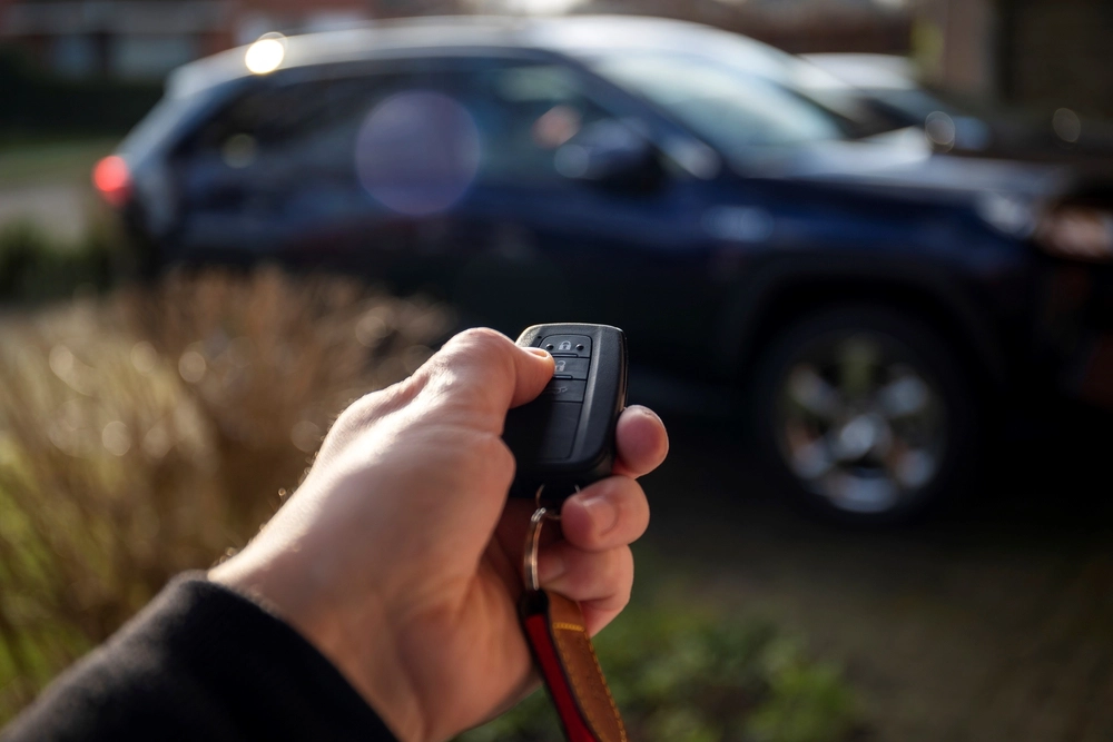 A close up portrait of a person holding a car key in his hand pressing the unlock button
