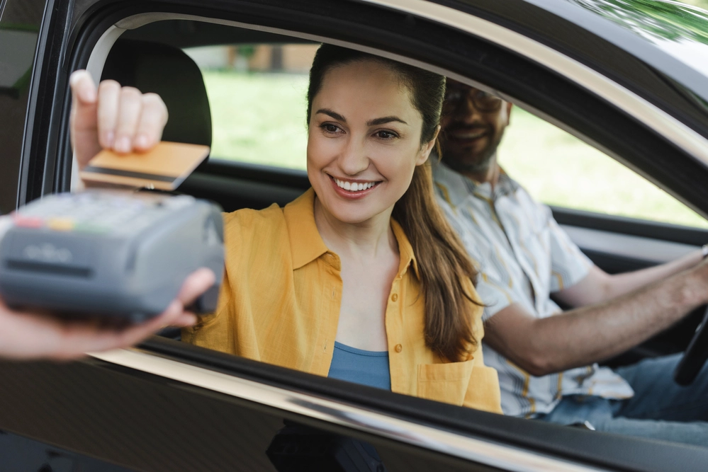 Selective focus of smiling woman paying with credit card near husband in car